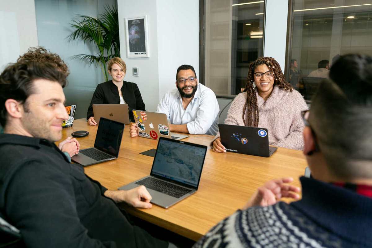 four-people-all-on-laptops-two-men-and-two-women-listen-to-person-talking-in-a-board-meeting-ZT5v0puBjZI