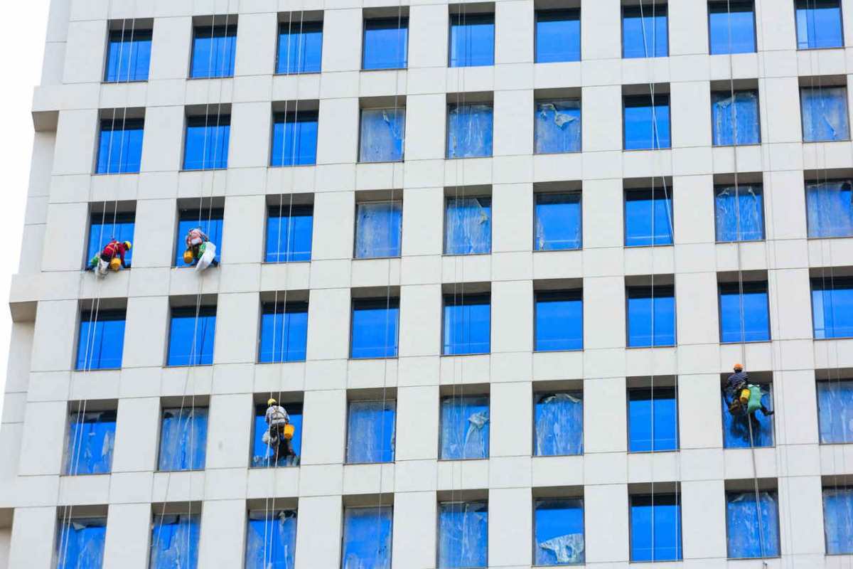 Professional workers clean skyscraper windows using ropes in urban setting.