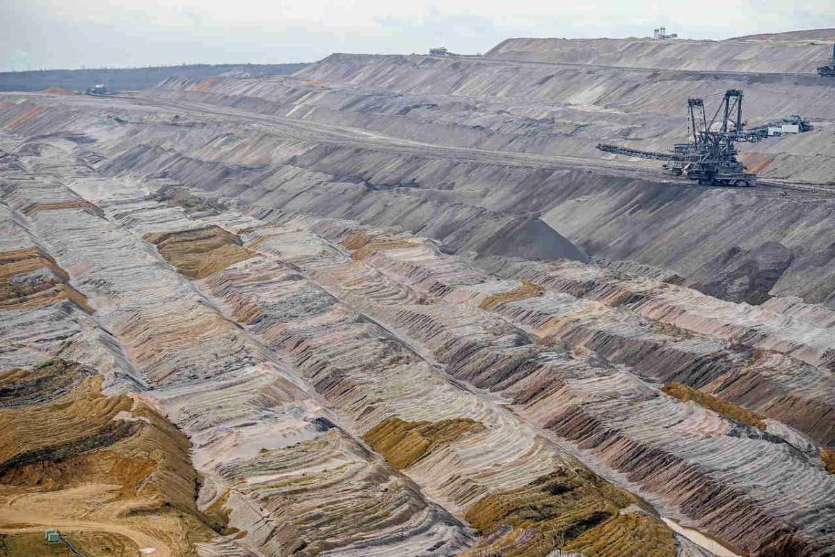 Aerial view of a large, barren open-pit mine featuring machinery and textured soil layers.