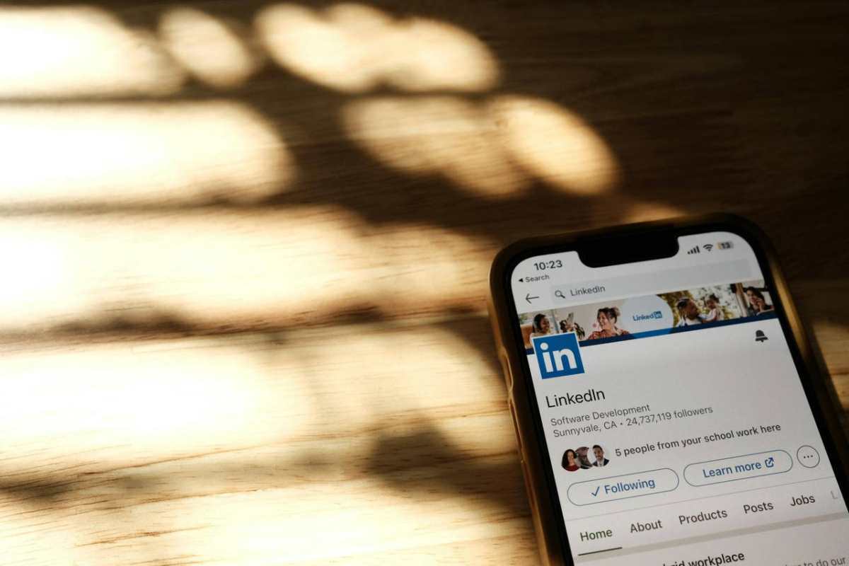 Close-up of a smartphone showing a LinkedIn profile page on a wooden table with shadows.