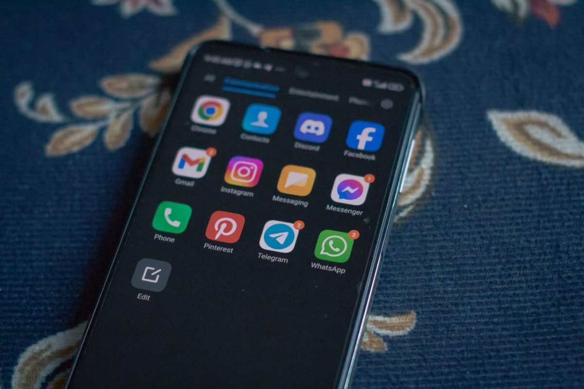 Close-up of a smartphone displaying popular social media apps on a floral fabric surface.