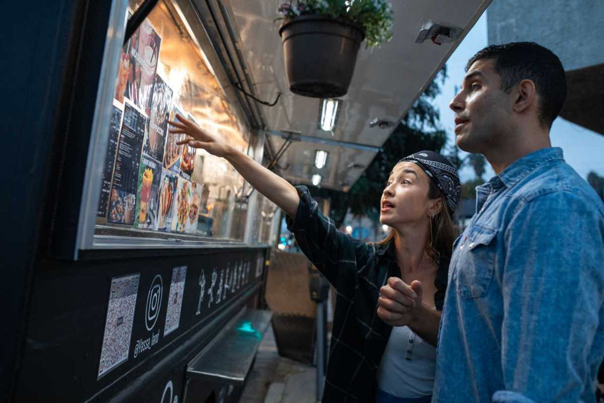 A couple choosing food from a vibrant street food truck menu during the evening.