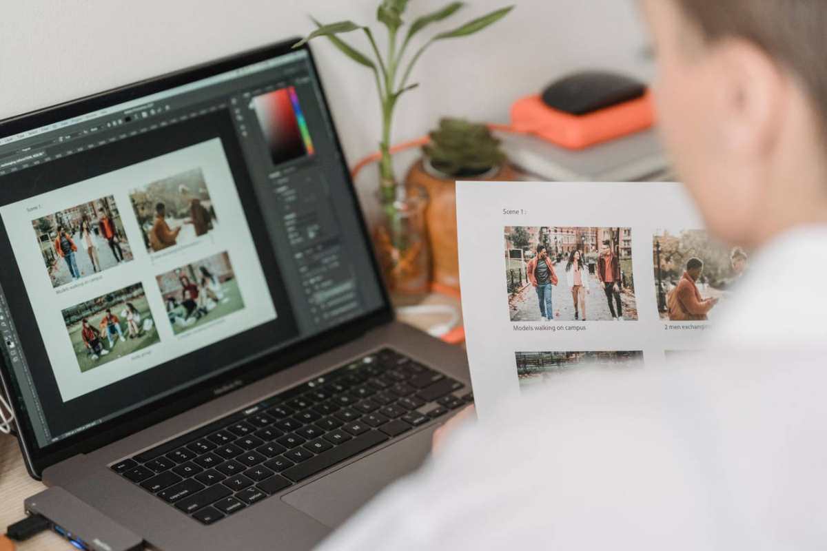 High angle of crop female photographer sitting at table with laptop and printed photoshoot while working remotely