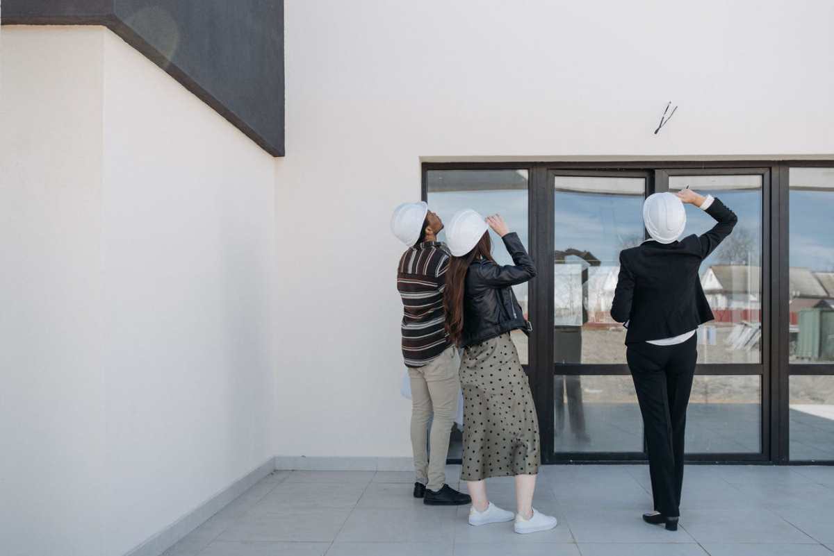 Three architects evaluating exterior building structure, wearing helmets and business attire.
