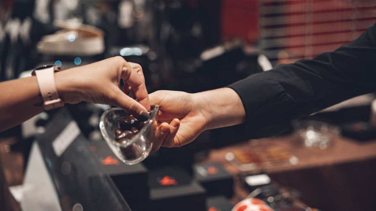Close-up of two people exchanging chocolates in a store setting.