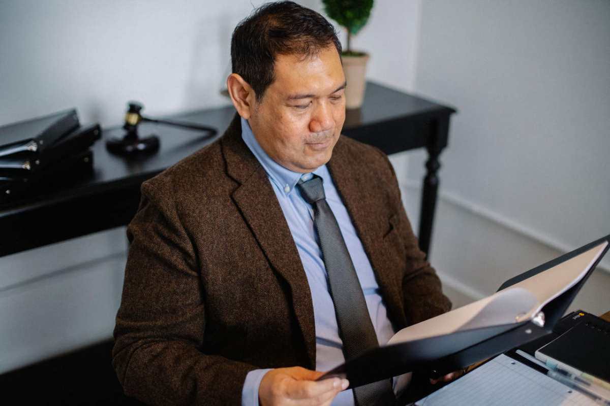 From above of serious ethnic lawyer in elegant suit checking report in folder on blurred background of office