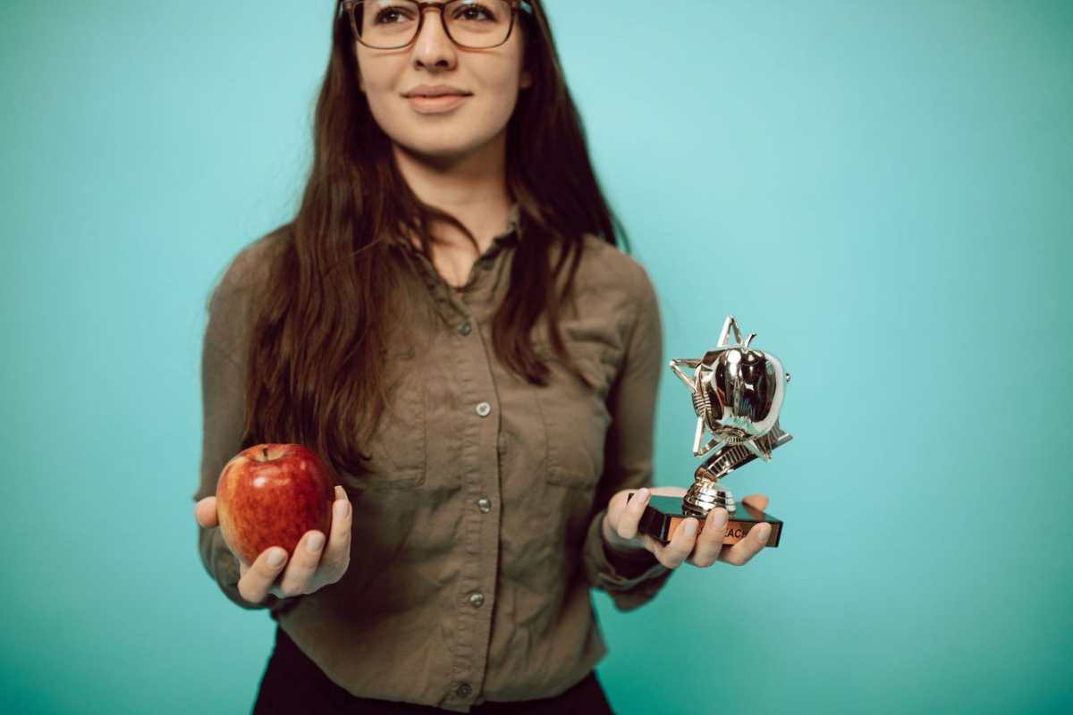 Woman holding an award trophy and apple against a turquoise background, symbolizing achievement and balance.