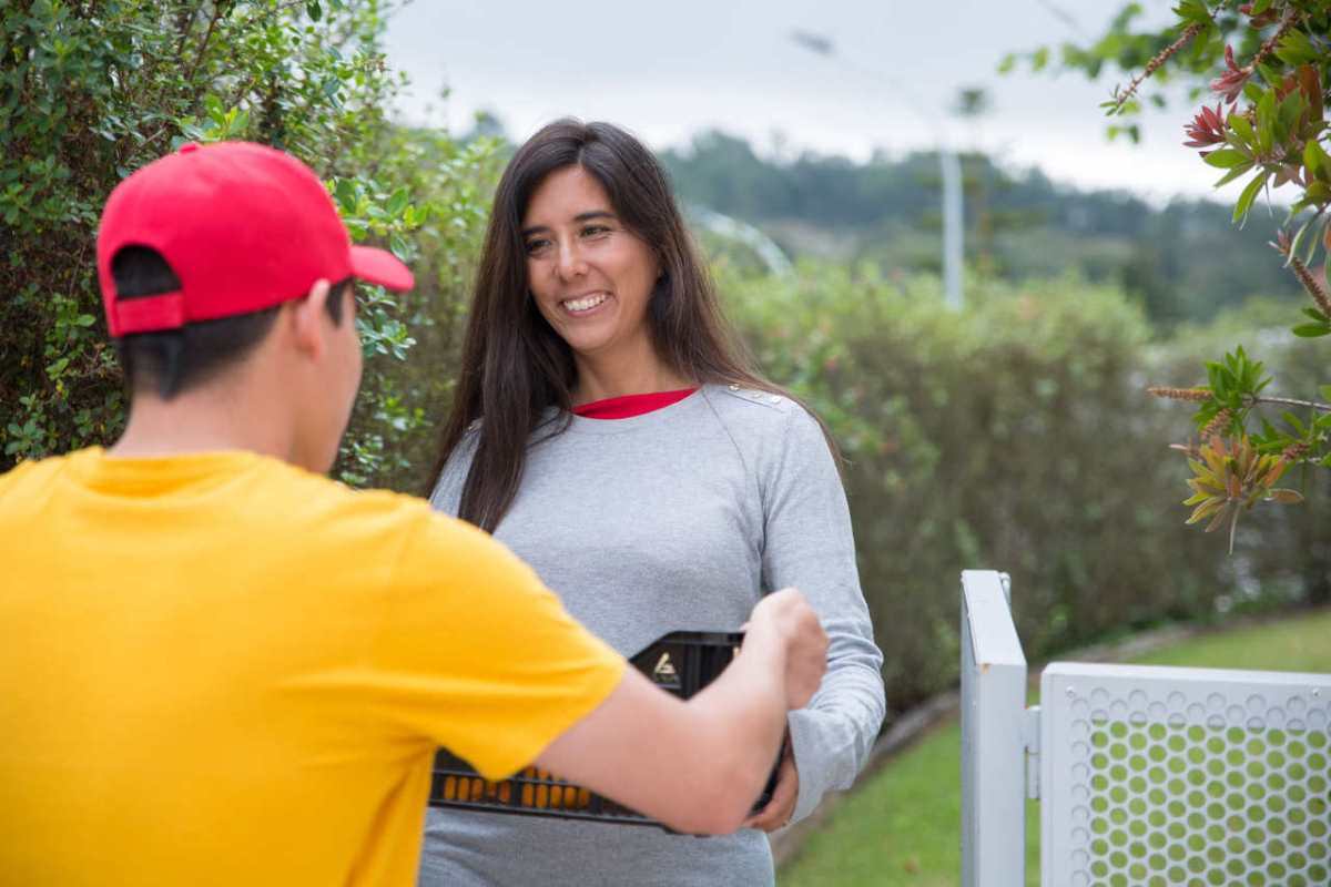 Smiling woman receives a package from a delivery man in a residential area outdoors.