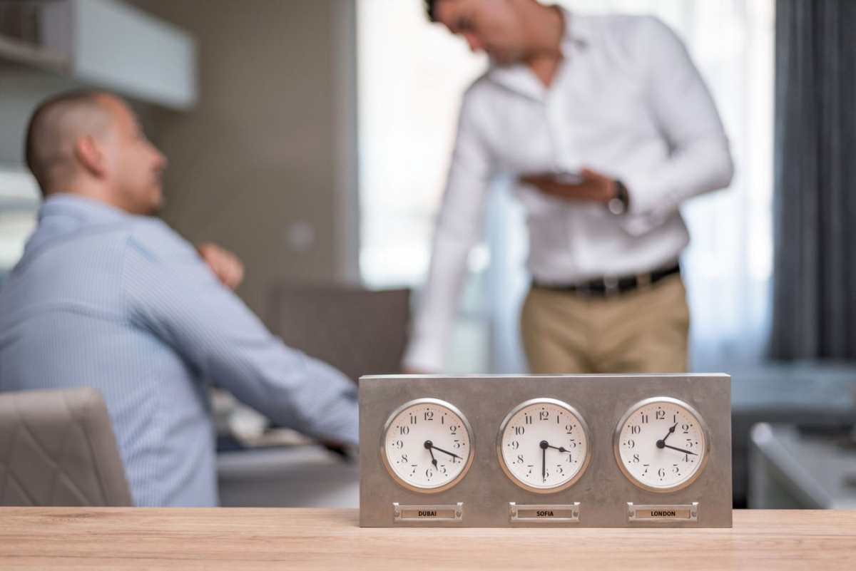 Two businessmen in an office with clocks displaying Dubai, Sofia, London time.