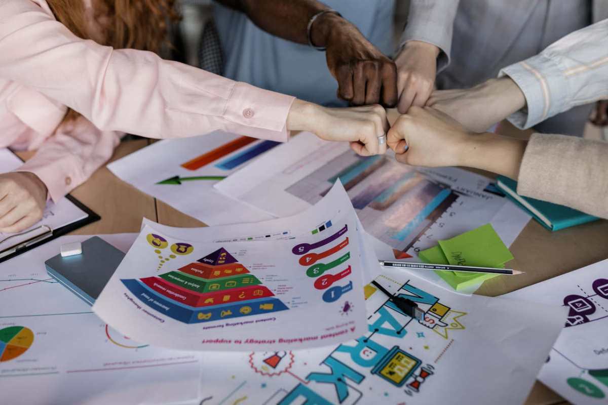 A diverse team unites hands over business reports and marketing strategies, symbolizing teamwork.