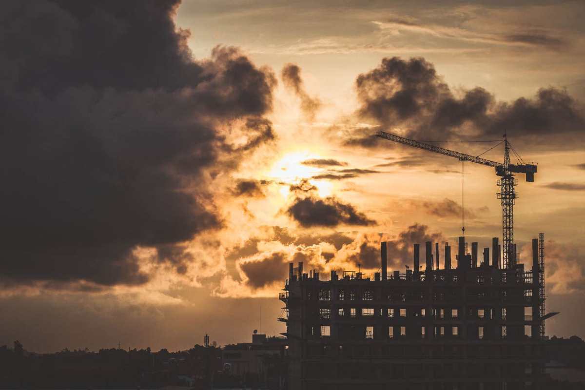 Silhouette of an unfinished building at sunset, featuring a construction crane and dramatic cloudscape.