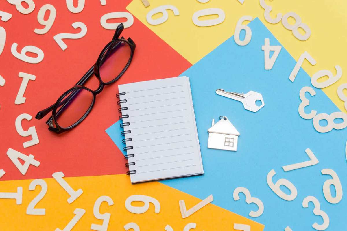Flat lay of a colorful desktop featuring a notebook, eyeglasses, and house key with numbers scattered.