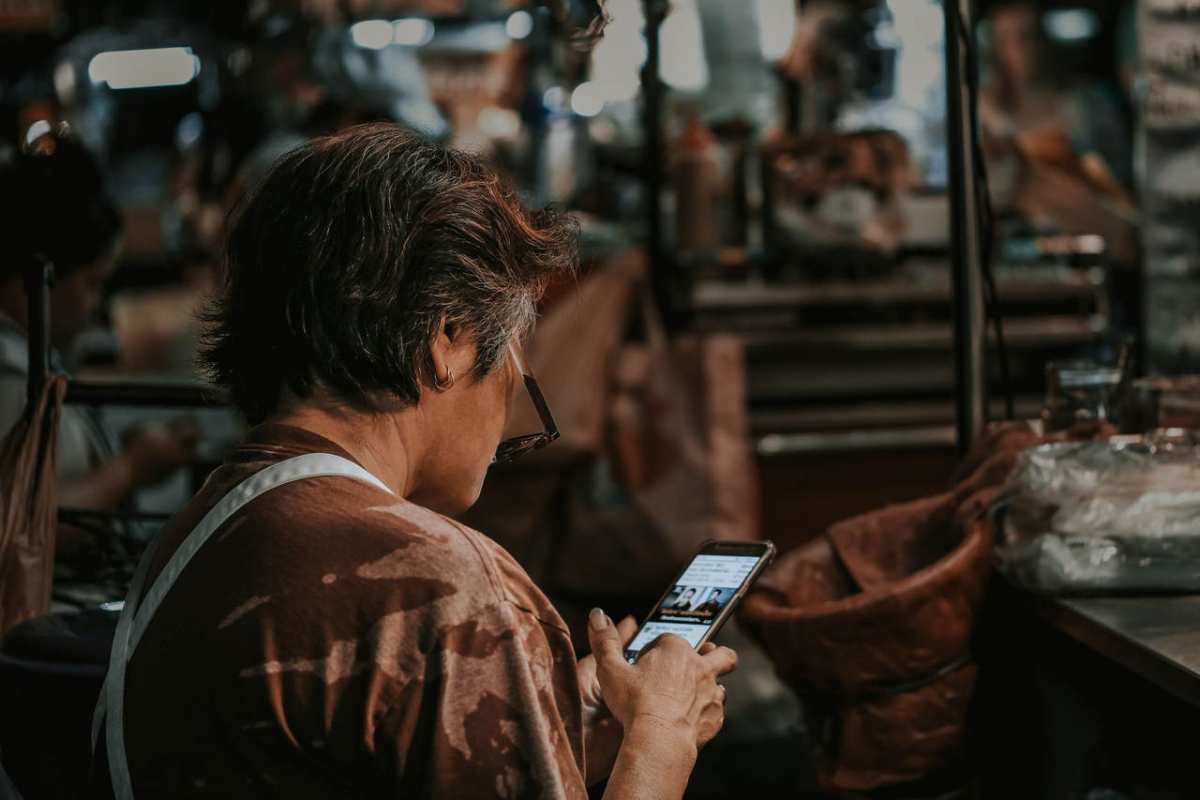 A woman with short hair looking down at a smartphone in a busy market environment.