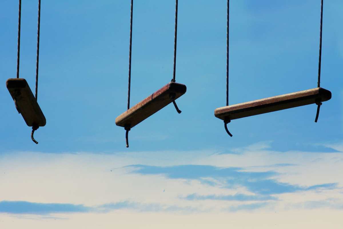 Three rustic swings suspended against a clear blue sky create a nostalgic scene.