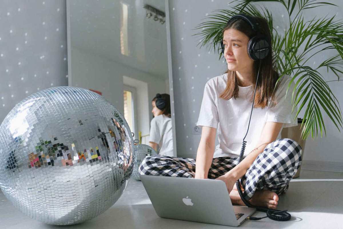 A young woman working from home, using a laptop and headphones, surrounded by a disco ball and plants.