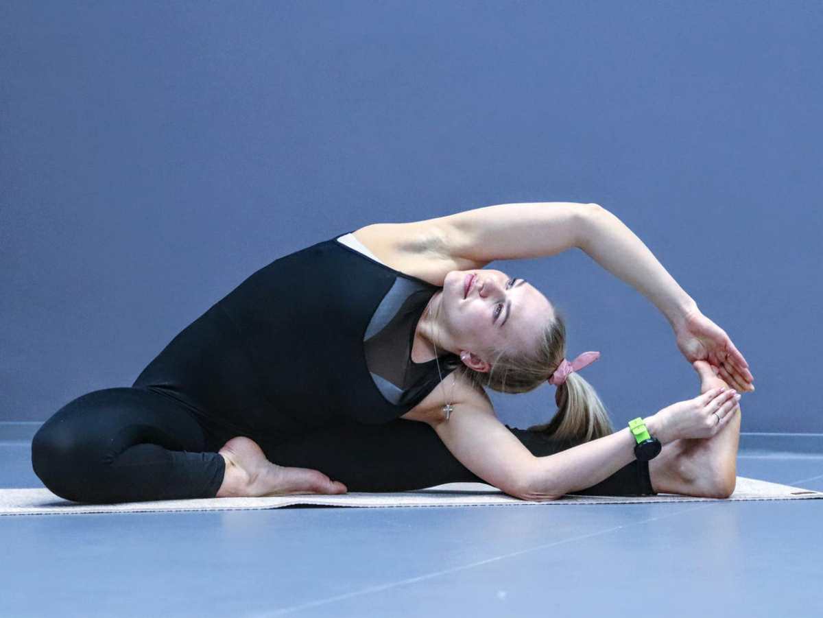 Flexible woman performing a yoga stretch indoors on a mat, promoting fitness and balance.