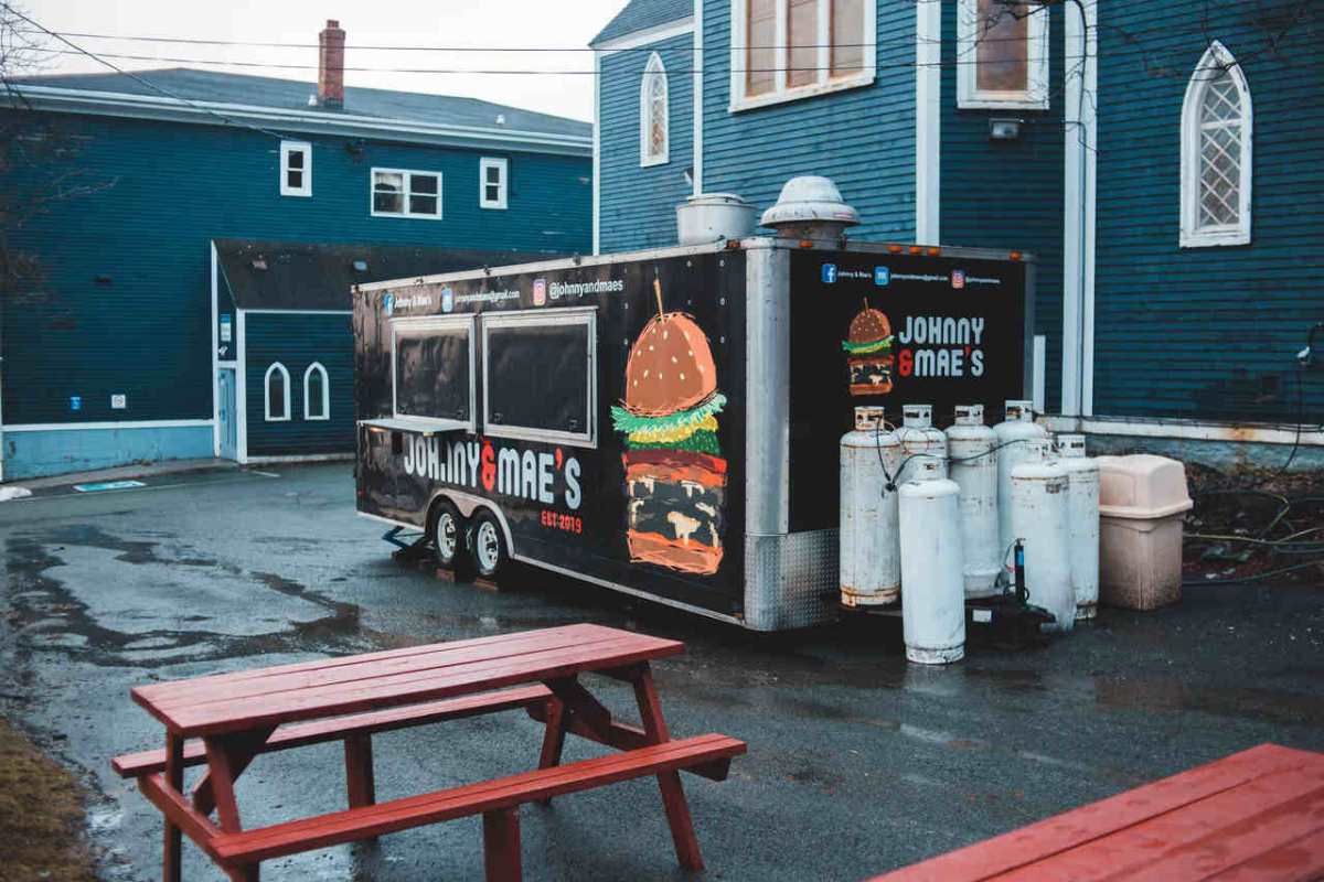 From above of food truck placed on wet asphalt area with wooden tables and benches in front of blue buildings