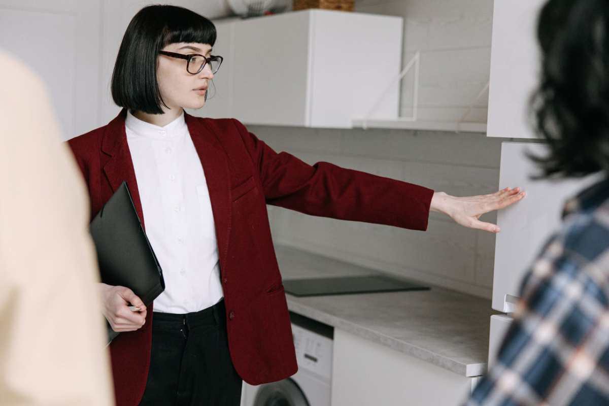 A female real estate agent demonstrates a modern kitchen to potential buyers in an apartment.