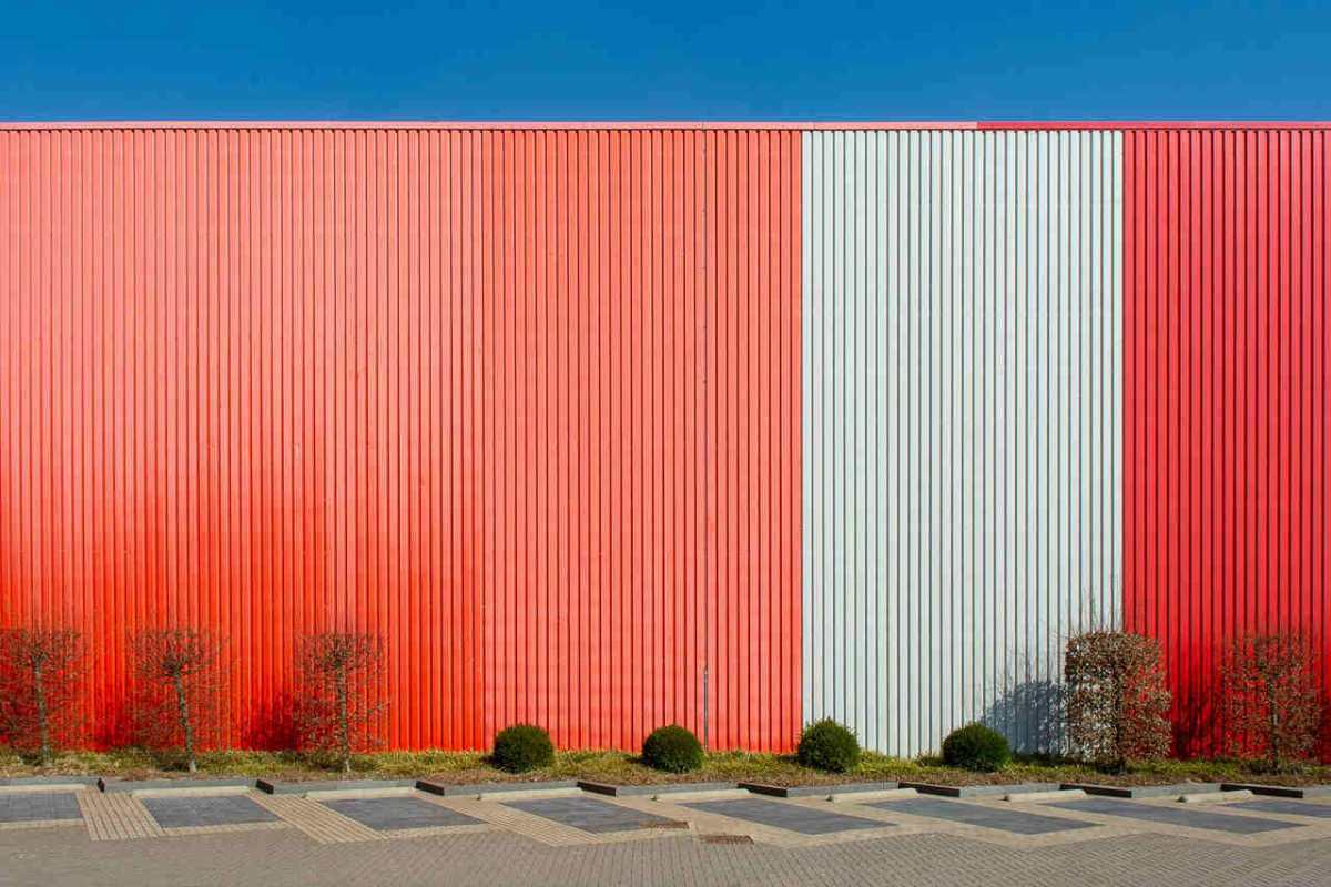 A vibrant red and white paneled wall of an industrial building with clear blue sky.