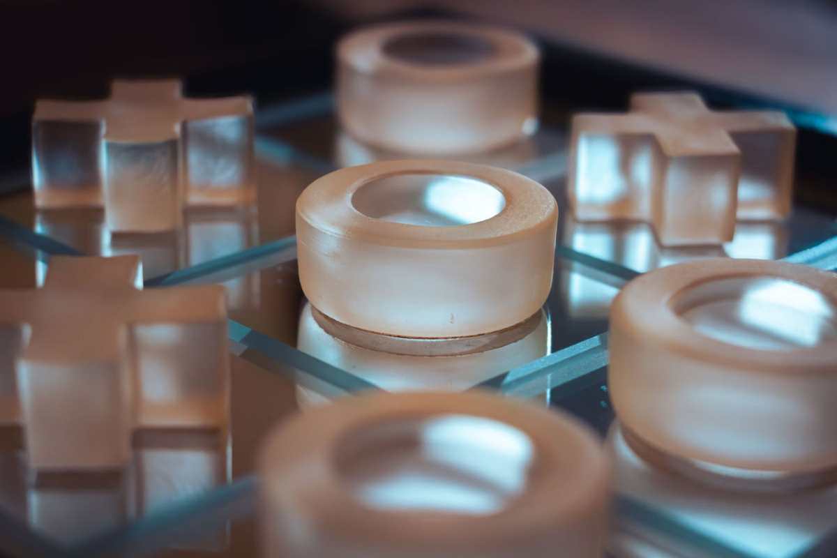 Close-up of a modern glass tic-tac-toe board with circular and cross pieces.