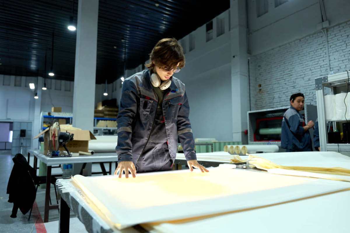 Worker in uniform examining sheets in a brightly lit factory environment, focusing on quality.