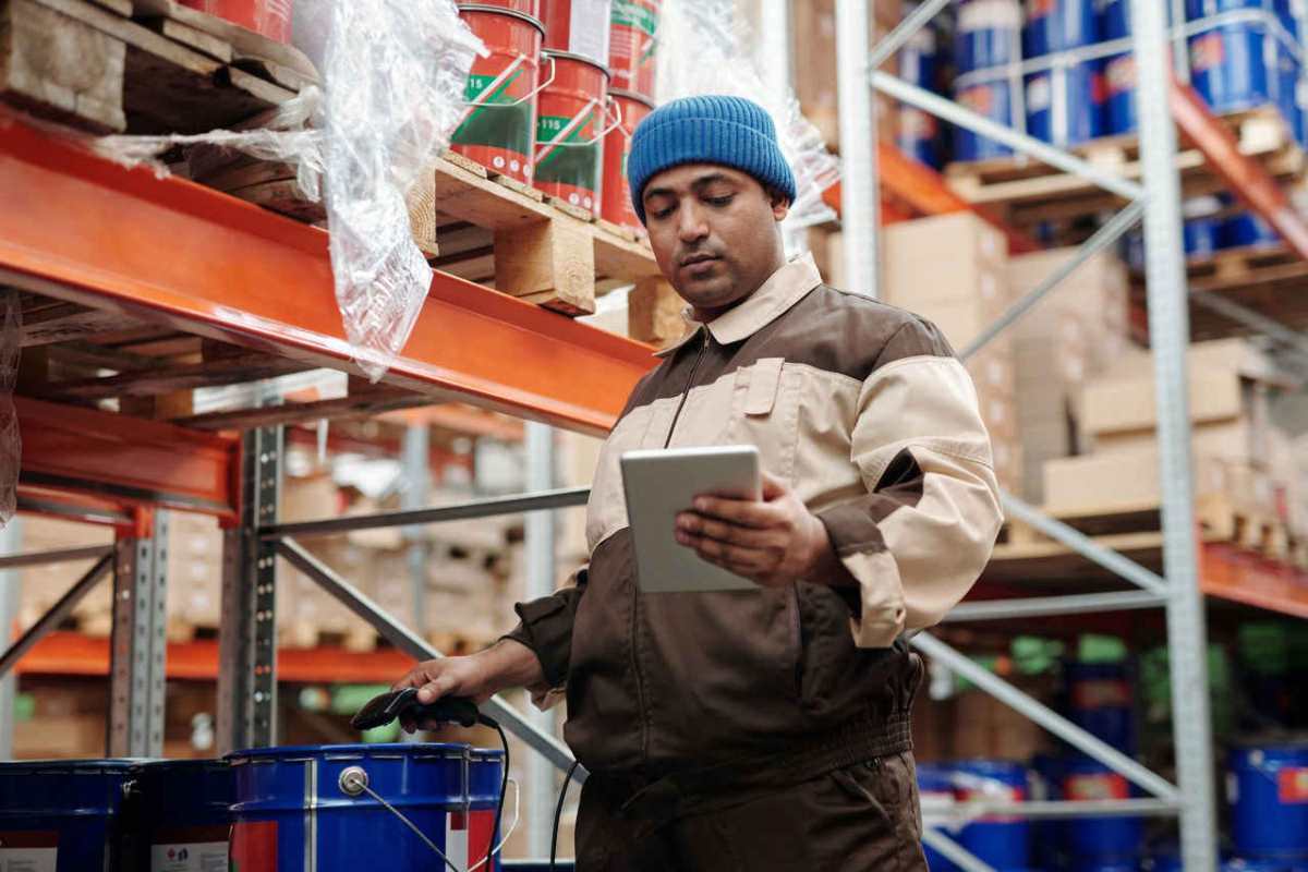 Man in blue beanie uses tablet in a warehouse for inventory management.