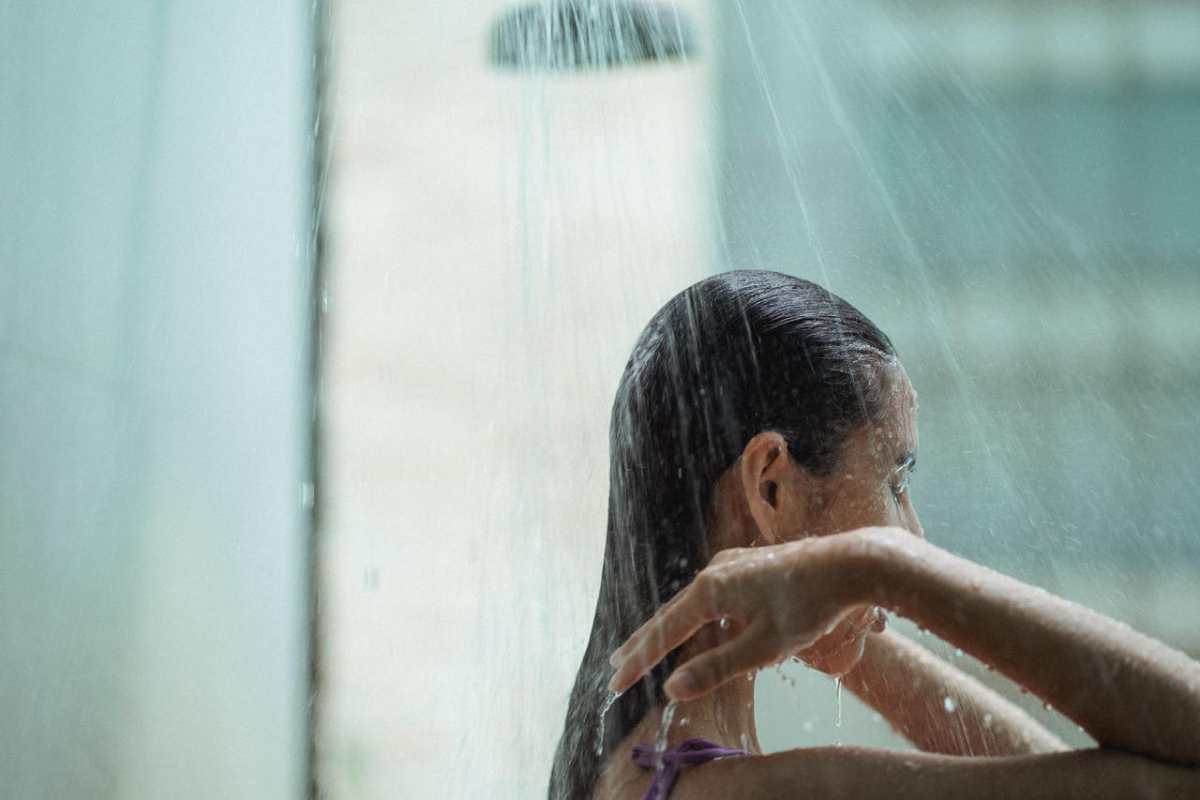 Side view of lady with closed eyes standing in shower and enjoying water