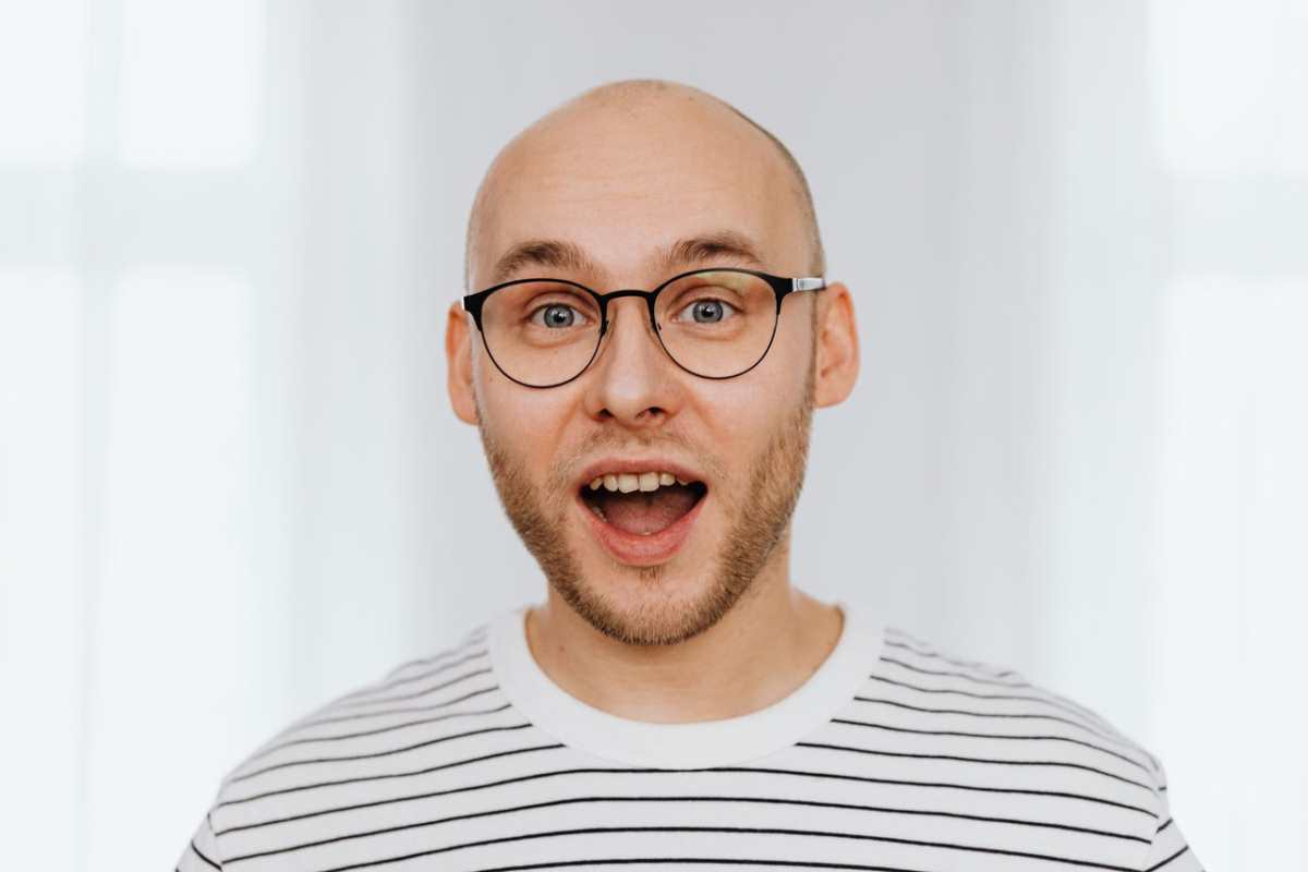 A bald man with glasses showing a surprised expression indoors, wearing a striped shirt.