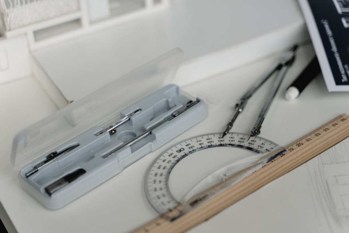 Close-up of architectural drafting tools including compasses, ruler, and paper on a workspace table.