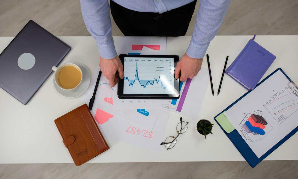 Overhead view of businessman using tablet to review data charts at a modern office desk.