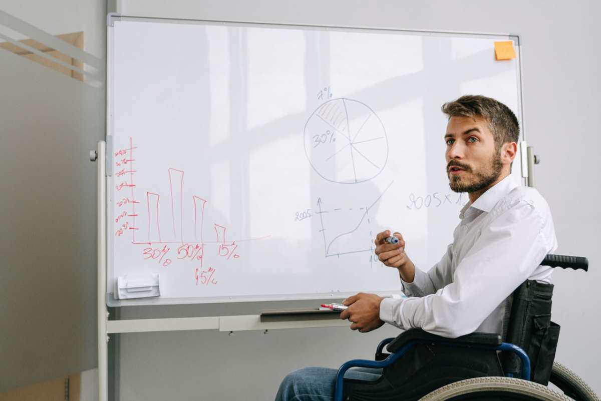 Businessman in wheelchair presenting data analysis on a whiteboard in office.